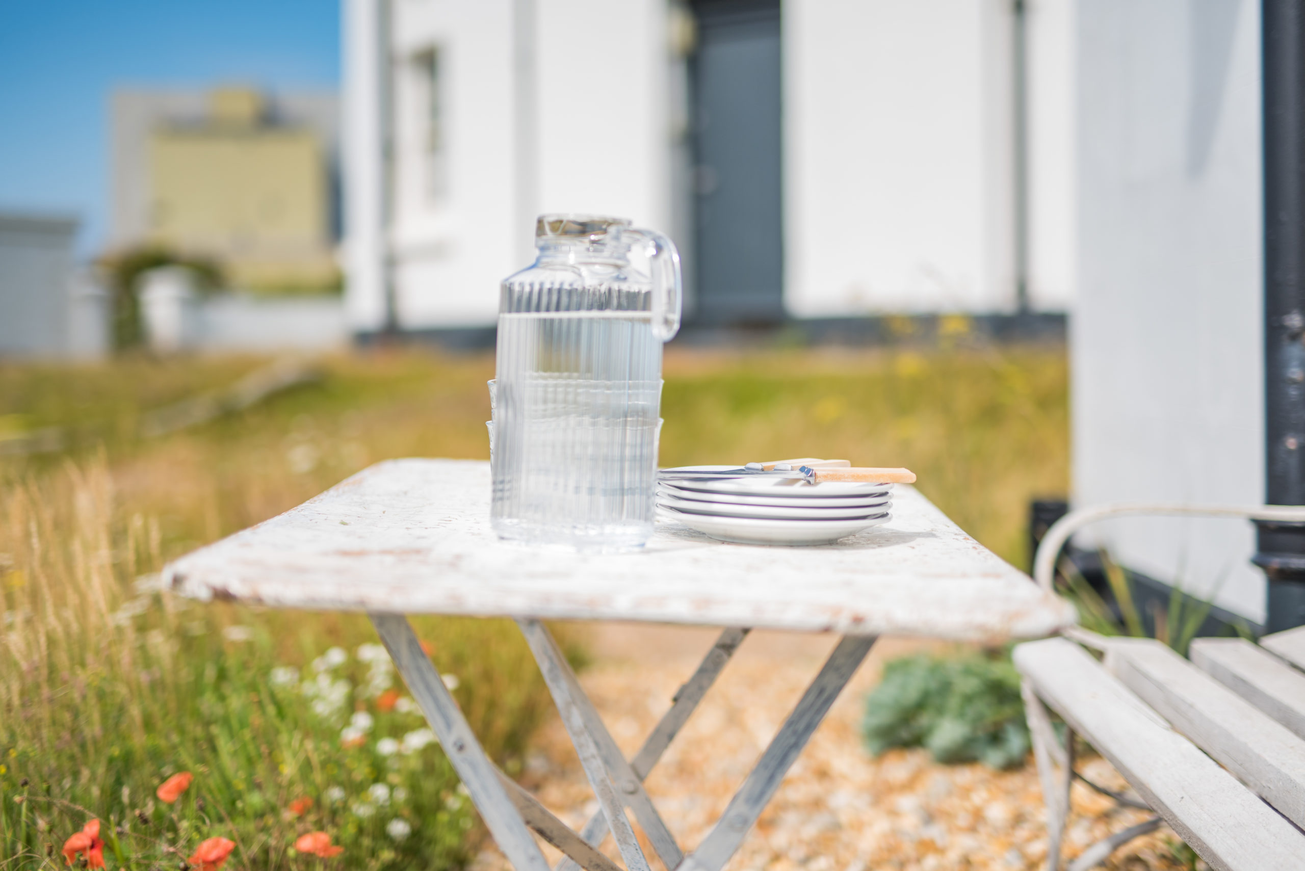 A summery outside table with a jug of water and stack of plates