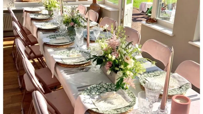 A sunny conservatory with a beautifully laid table set for dinner with flowers in the middle to compliment the neutral colours. Set up by Beyond The Table.