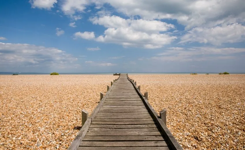 Boardwalk stretching toward the sea on a pebble beach, cumulus overhead in beautiful summer sky. Romney Marsh, Kent, England.