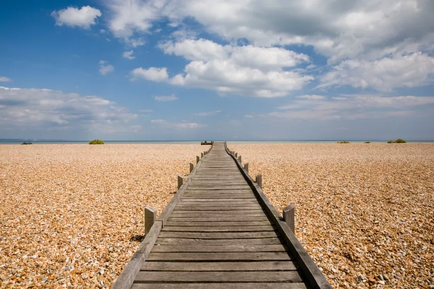Boardwalk stretching toward the sea on a pebble beach, cumulus overhead in beautiful summer sky. Romney Marsh, Kent, England.