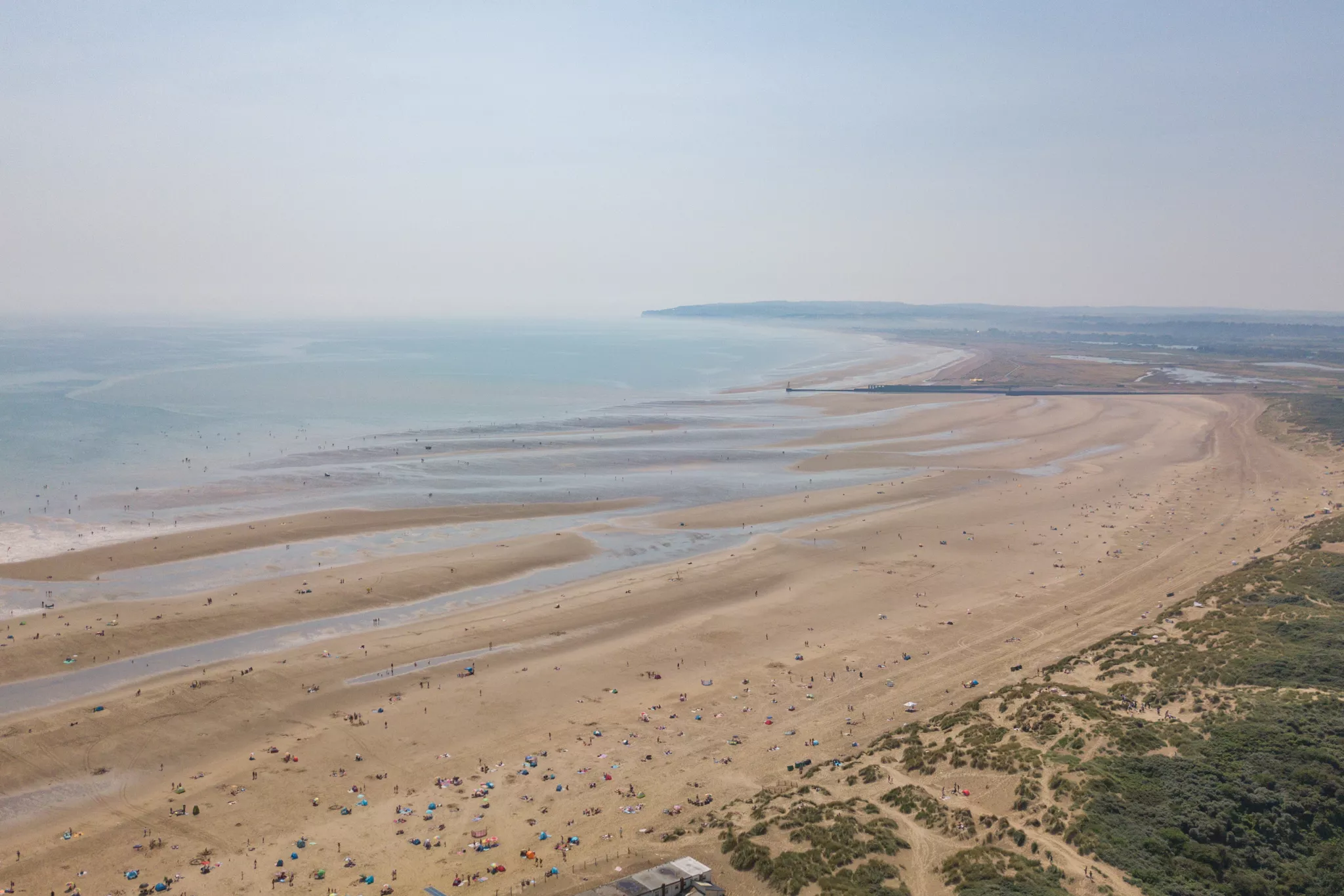 The wide open beach at Camber Sands in Sussex, the tide is far out and there's people on the beach.