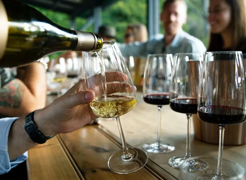 English white wine being poured into a wine glass, with red wine in front ready for guests to taste