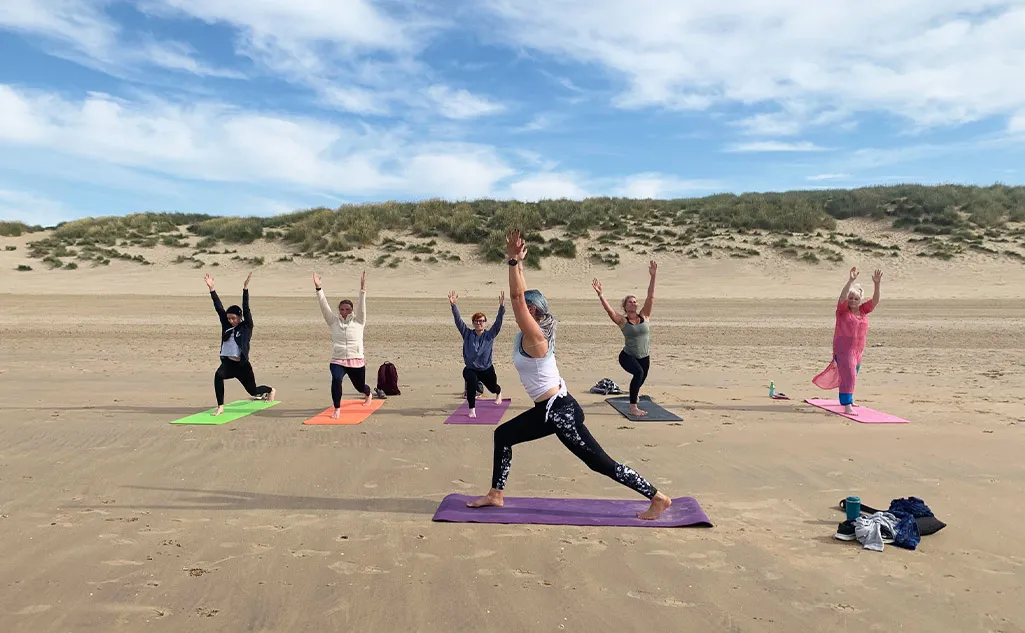 A group of women enjoying a yoga class on a Kent beach, led by Jo Humble Warrior a Yoga Teacher