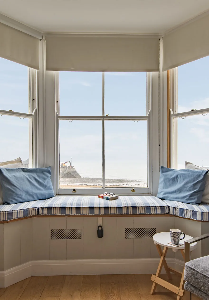 A cosy window seat that looks out to sea, set with a book and coffee mug.