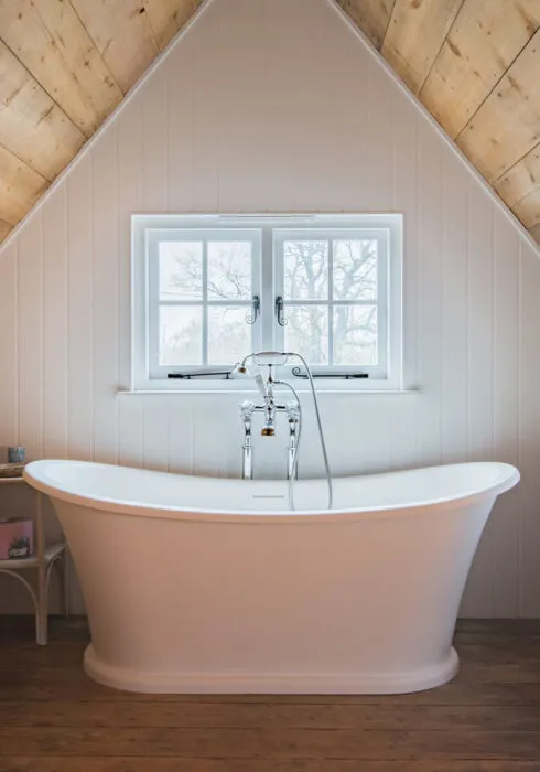 A white roll top bath positioned in front of two windows at Bushes Oast, a holiday cottage