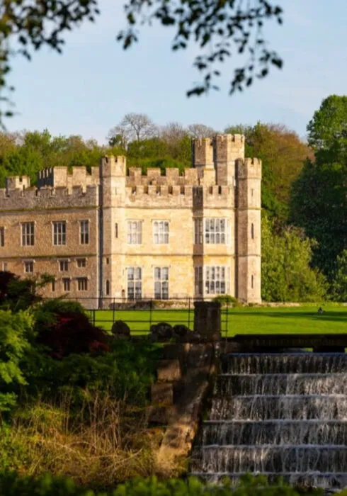 An external photo of Leeds Castle in the sun with the waterfall in front of it.