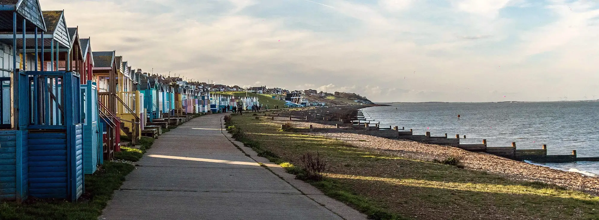 A landscape photo capturing the sunset at Whitstable, focusing on the colourful beach huts, pebbly beach and the tide coming in.
