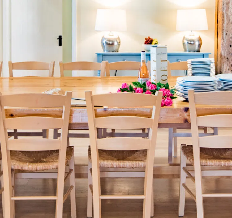 The large, open-plan dining area of Great Higham Barn in Doddington near Faversham. The table is left unlaid with a stack of plates, pink roses and prosecco ready for guests.