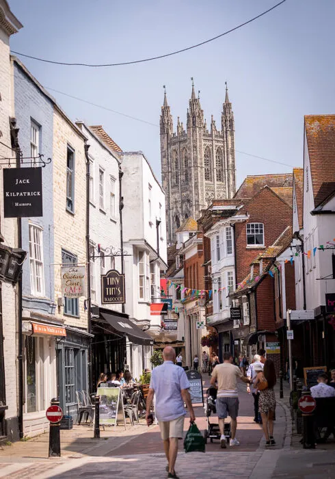 A portrait photo of a narrow street in Canterbury, involving cafes and the Cathedral in the background.