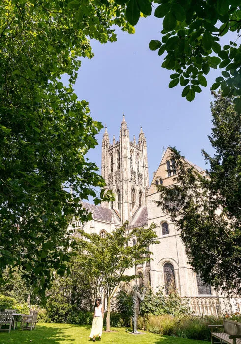 A portrait photo of Canterbury cathedral in the sunshine framed by green leaves on the trees.