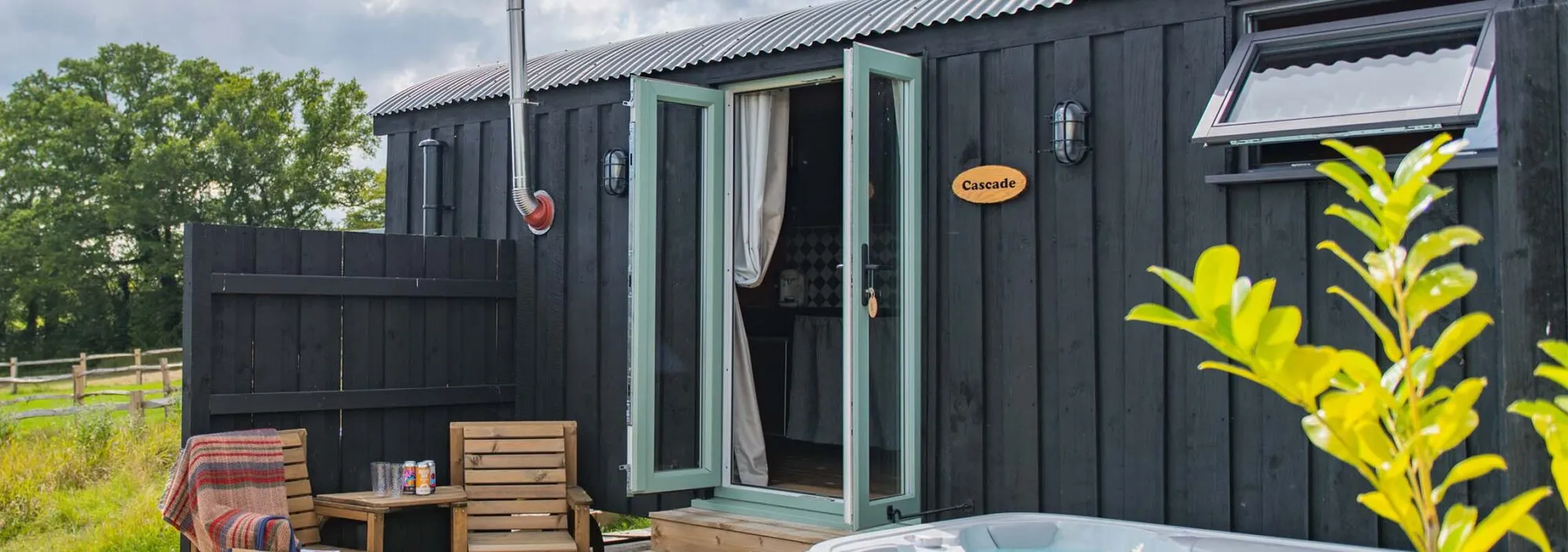 Photo of a cabin with a hot tub and chairs positioned outside on the decking of Cascade, a holiday home on Mccann's Brewery in Tenterden.