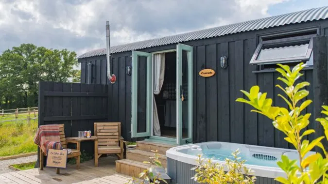 Photo of a cabin with a hot tub and chairs positioned outside on the decking of Cascade, a holiday home on Mccann's Brewery in Tenterden.