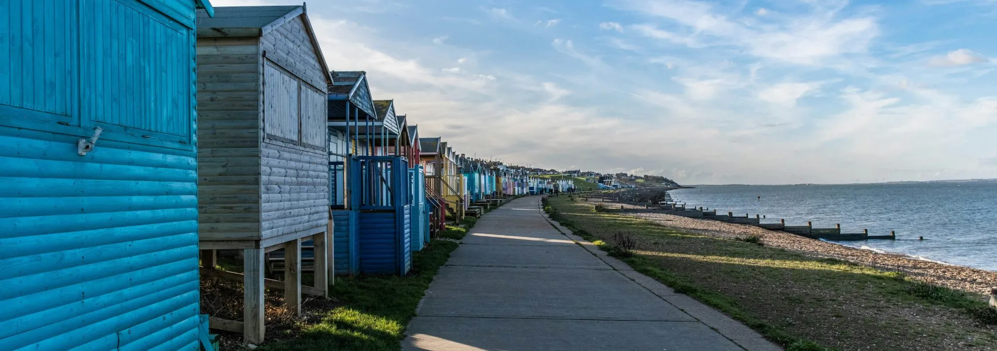 Whitstable beach, showing the town's famous beach huts on the left of the promenade (facing west), and the beach and ocean to the right