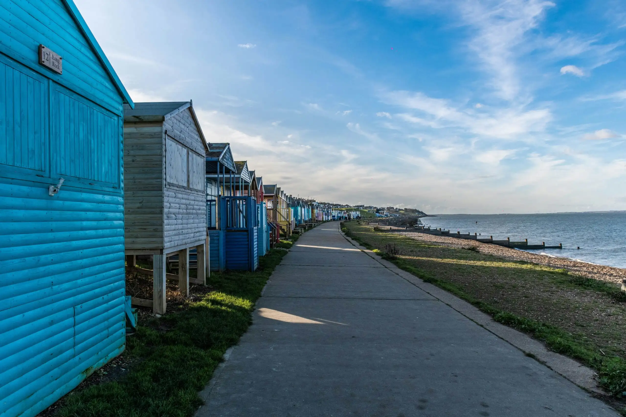 Whitstable beach, showing the town's famous beach huts on the left of the promenade (facing west), and the beach and ocean to the right