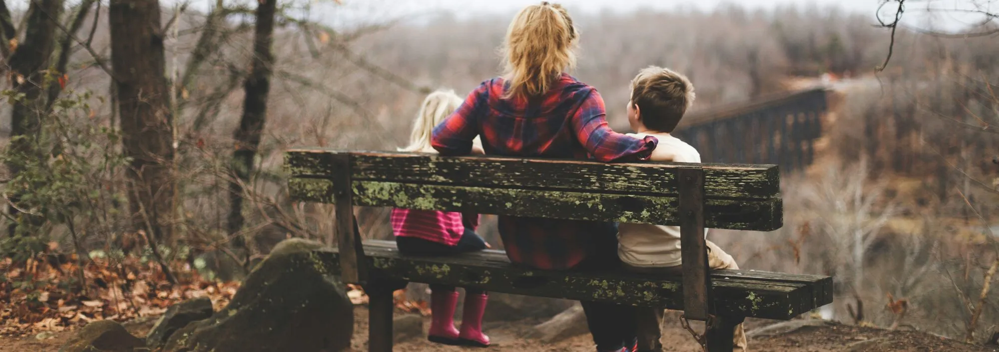 Picture shows a woman sitting with two young children on a bench, overlooking the forested area ahead of them.