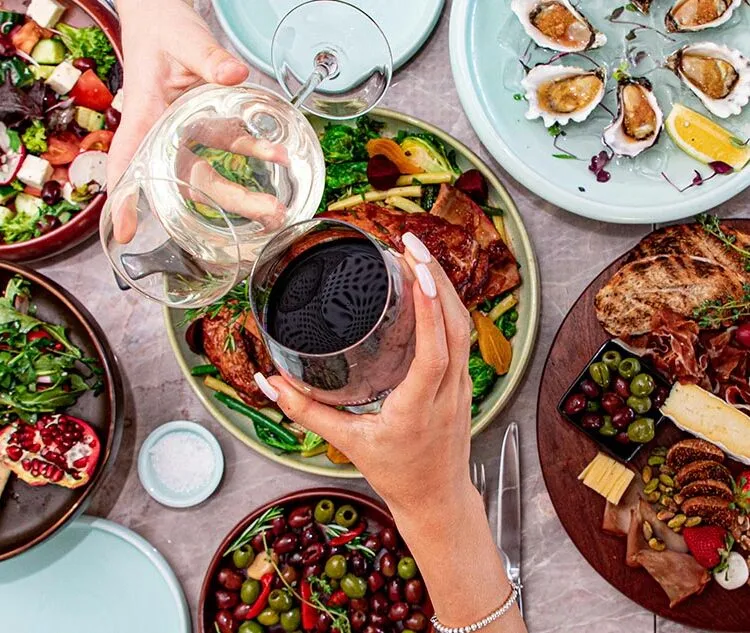 A dinner table set with lovely vibrant food and people raising a glass of wine
