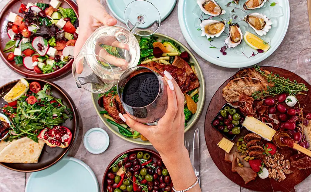 A dinner table set with lovely vibrant food and people raising a glass of wine